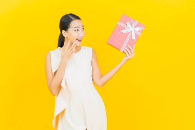 Asyalı güzel bir kadının portresi. Sarı arka planda kırmızı hediye kutusuyla gülümsüyor.