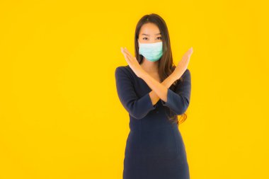 Koronavirüsten korunmak için maske takmış güzel Asyalı bir kadın portresi ve sarı izole edilmiş arka planda 19 numara.