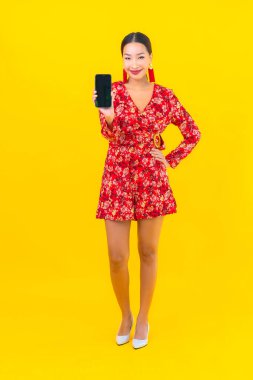 Güzel bir Asyalı kadın. Sarı arka planda akıllı cep telefonu kullanıyor.