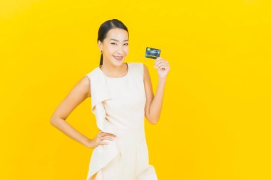 Asyalı güzel bir kadının portresi. Sarı arka planda kredi kartıyla gülümsüyor.