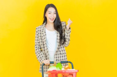 Renkli arka planda süpermarketten alınmış market sepetiyle gülümseyen güzel Asyalı kadın portresi.