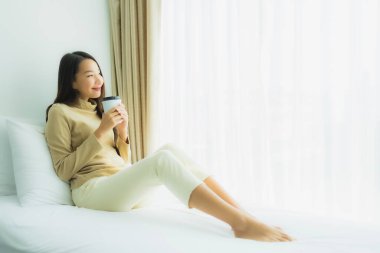 Yatak odasının iç tarafında, kahve fincanı olan Asyalı genç bir kadın.