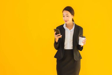 Portre güzel genç Asyalı kadın akıllı cep telefonu ve kahve fincanı ile izole edilmiş sarı arka planda