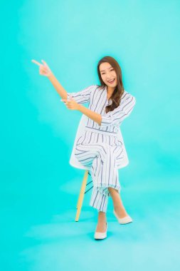 Asyalı güzel bir kadının portresi gülümse ve mavi izole edilmiş arka planda bir sandalyeye otur.