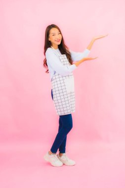 Portrait beautiful young asian woman in kitchen wear with apron on pink isolated background