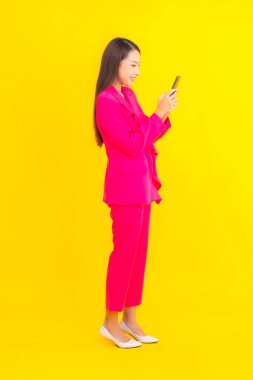 Güzel bir Asyalı kadın portresi sarı renkli izole edilmiş arka planda akıllı cep telefonu kullanır.