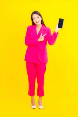 Güzel bir Asyalı kadın portresi sarı renkli izole edilmiş arka planda akıllı cep telefonu kullanır.