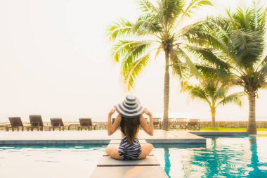 Güzel bir Asyalı kadın portresi, gün batımında palmiye ağacıyla birlikte havuz kenarında dinleniyor ya da tatil için gün doğumunda dinleniyor.