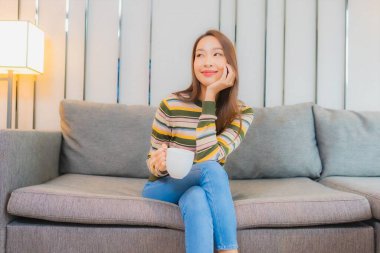 Güzel bir Asyalı kadın portresi. Oturma odasındaki kanepede rahatça gülümse.