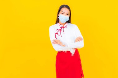 Güzel bir Asyalı kadın portresi maske takıyor ve sarı arka planda Covid19 'u korumak için alkol jeli kullanıyor.