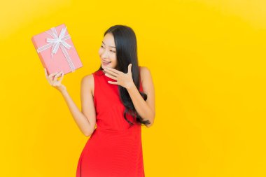 Asyalı güzel bir kadının portresi. Sarı arka planda kırmızı hediye kutusuyla gülümsüyor.