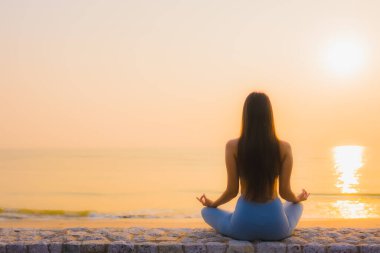 Genç Asyalı kadının portresi sağlık için gün doğumunda deniz kıyısı okyanusunda meditasyon yapıyor.