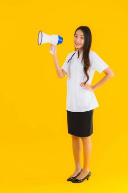 Güzel bir Asyalı genç doktor portresi. Sarı izole arka planda megafon kullanıyor.