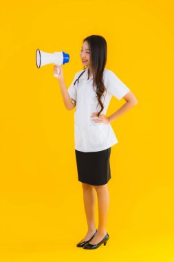 Güzel bir Asyalı genç doktor portresi. Sarı izole arka planda megafon kullanıyor.