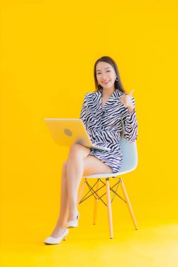 Güzel bir Asyalı kadın, sarı izole edilmiş arka planda dizüstü bilgisayar kullanıyor.