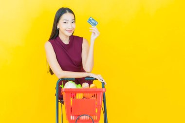 Renkli arka planda süpermarketten alınmış market sepetiyle gülümseyen güzel Asyalı kadın portresi.