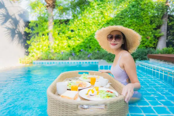 Genç Asyalı kadının portresi mutlu bir gülümseme ile otel havuzunda yüzen kahvaltı tepsisinin keyfini çıkar.