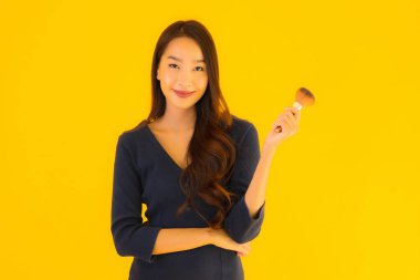 Sarı izole arkaplanda makyaj fırçası olan güzel bir Asyalı kadın portresi.