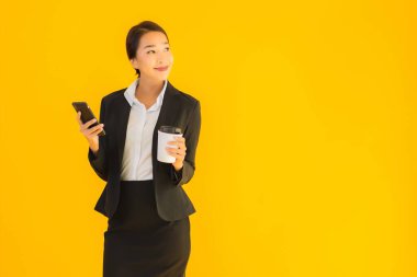 Portre güzel genç Asyalı kadın akıllı cep telefonu ve kahve fincanı ile izole edilmiş sarı arka planda