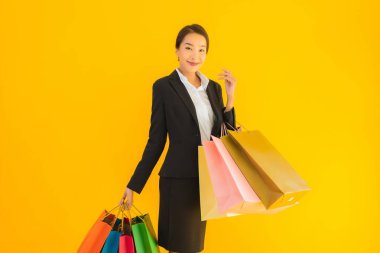 Sarı izole edilmiş arka planda alışveriş merkezinden alışveriş çantasıyla güzel bir genç Asyalı kadın portresi.