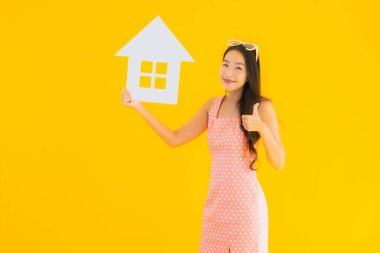 Güzel genç Asyalı kadın sarı izole arka planda ev ya da ev tabelasını gösteriyor.