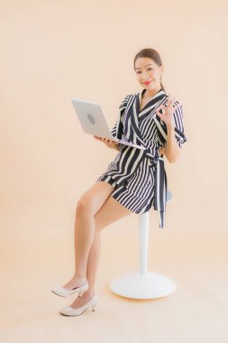 Kahverengi arka planda dizüstü bilgisayarı olan güzel bir Asyalı kadın portresi.