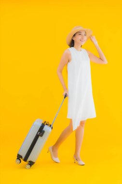 Güzel genç Asyalı kadın portresi, sarı izole arka planda valizli seyahat kavramı.
