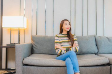 Güzel bir Asyalı kadın portresi. Oturma odasındaki kanepede rahatça gülümse.