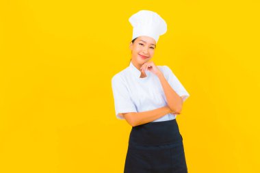 Güzel bir Asyalı kadın portresi ya da sarı izole arkaplanda şapkası olan aşçı üniforması.