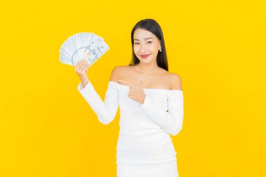 Bir sürü parası ve sarı arka planda kumbarası olan Asyalı güzel bir iş kadını portresi.