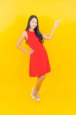 Güzel bir portre genç Asyalı kadın kırmızı elbiseler giyip sarı arka planda hareketli bir gülümseme takın.