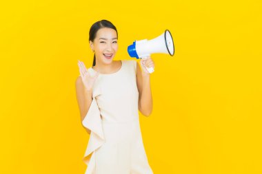 Asyalı güzel bir kadının portresi sarı arka planda megafonla gülümsüyor.