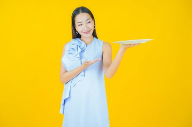 Güzel Asyalı bir kadının portresi. Arka planda boş tabak tabağıyla gülümsüyor.