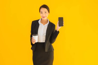 Portre güzel genç Asyalı kadın akıllı cep telefonu ve kahve fincanı ile izole edilmiş sarı arka planda