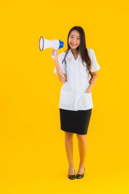 Güzel bir Asyalı genç doktor portresi. Sarı izole arka planda megafon kullanıyor.