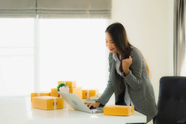 Güzel Asyalı iş kadını portresi evden bilgisayarlı cep telefonuyla karton kutuyla çevrimiçi alışveriş için hazır bekliyor.
