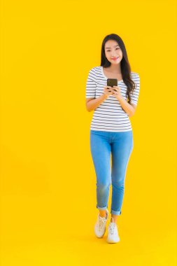 Güzel bir Asyalı kadın portresi sarı izole edilmiş arka planda akıllı cep telefonu kullanıyor.