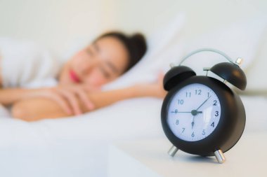 Portre güzel genç Asyalı kadın yatak odasında saatle yatakta uyuyor.
