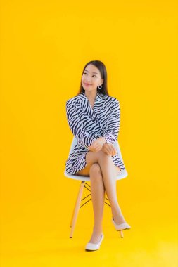 Güzel bir Asyalı kadın, sarı izole edilmiş arka planda hareketli bir şekilde sandalyede oturuyor.