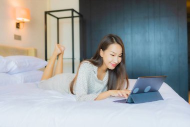 Güzel bir Asyalı kadının portresi yatak odasının içinde kredi kartıyla tablet kullanıyor.