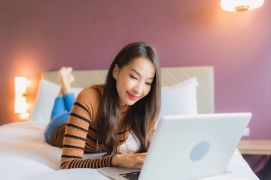 Asyalı güzel bir kadının portresi yatak odasının iç kısmında kredi kartıyla birlikte dizüstü bilgisayar kullanıyor.