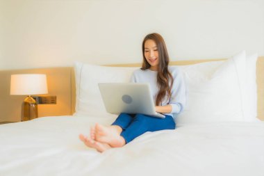 Güzel bir Asyalı kadın yatak odasının iç kısmında bilgisayar kullanıyor.