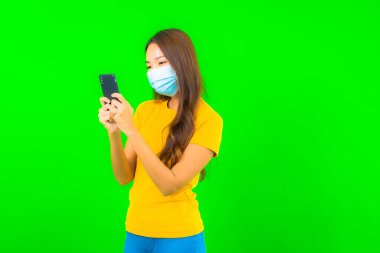 Güzel Asyalı genç bir kadının portresi, yeşil yalıtılmış arka planda kovid19 veya koronavirüsten korunmak için maske takar.