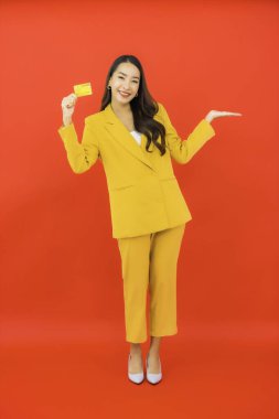 Güzel bir Asyalı kadının portresi kırmızı arka planda kredi kartıyla cep telefonu kullanıyor.