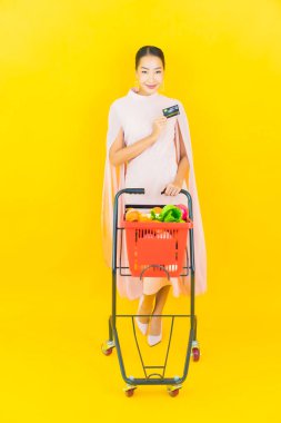 Sarı arka planda süpermarketten alınmış sepetli güzel Asyalı kadın portresi.