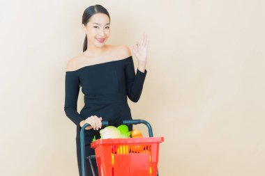 Renkli arka planda süpermarketten alınmış market sepetiyle gülümseyen güzel Asyalı kadın portresi.