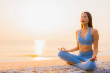 Genç Asyalı kadının portresi sağlık için gün doğumunda deniz kıyısı okyanusunda meditasyon yapıyor.