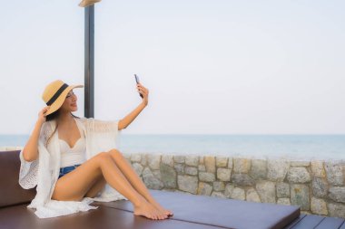 Açık deniz okyanusunda akıllı cep telefonu kullanan Asyalı genç bir kadının portresi.