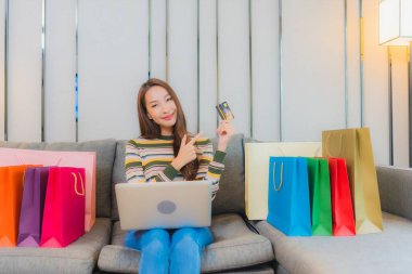 Asyalı güzel bir kadının portresi kanepeye dizüstü bilgisayar kullanıyor.