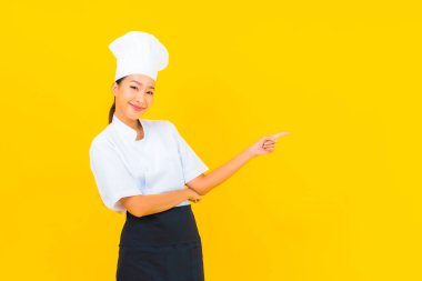 Güzel bir Asyalı kadın portresi ya da sarı izole arkaplanda şapkası olan aşçı üniforması.